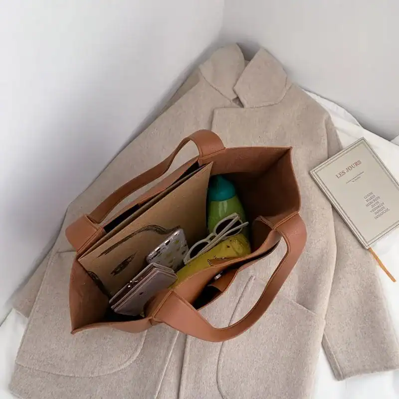 Svart tygshoppingväska med bruna handtag, fylld med vardagliga saker och placerad på en beige kappa.