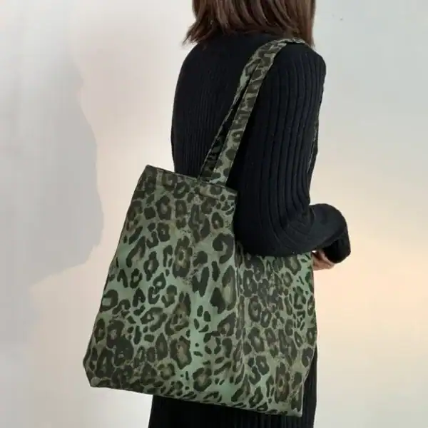 Grön axelväska med leopardmönster, bärs över axeln av kvinna i svart tröja.