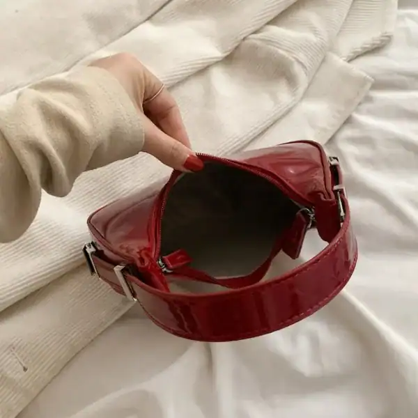 Vinröd lack halvmånsväska med silverfärgade snäckor och öppen ficka.