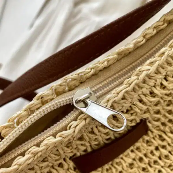 Virkad axelväska beige med metallisk dragkedja och brunt handtag.