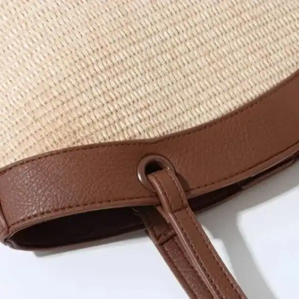 Vit beige stråväska med brunt läderband och handtag.