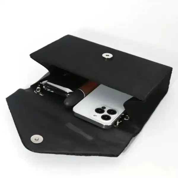 Svart glitterclutch med plattfodrad design, visar innehåll inklusive mobil och pennor.