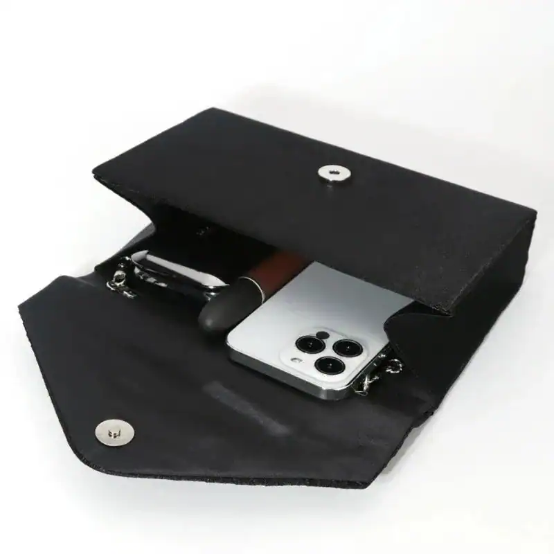 Svart glitterclutch med plattfodrad design, visar innehåll inklusive mobil och pennor.