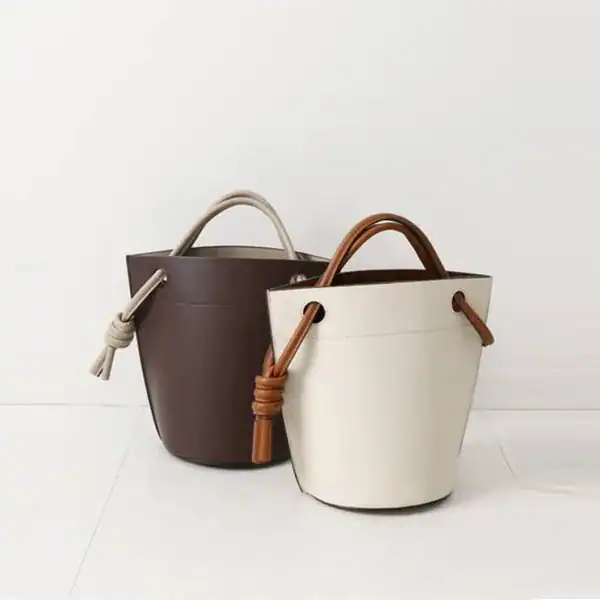 Vit och brun hinkväska i läder med handtag, minimalistiskt design.