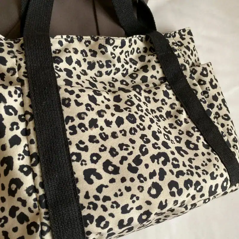 Vit leopardmönstrad väska med svarta handtag.