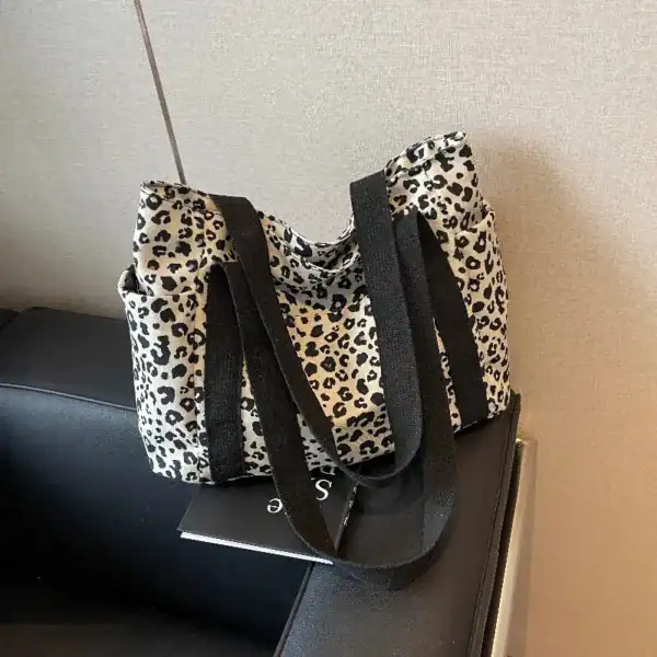 Vit leopard mönstrad axelväska med svarta handtag.