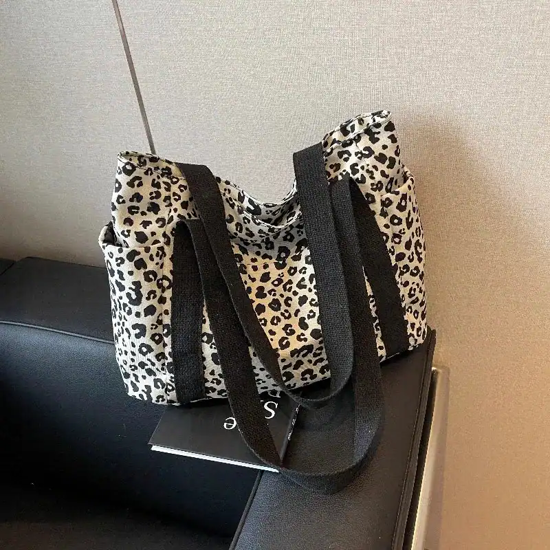 Vit leopard mönstrad axelväska med svarta handtag.