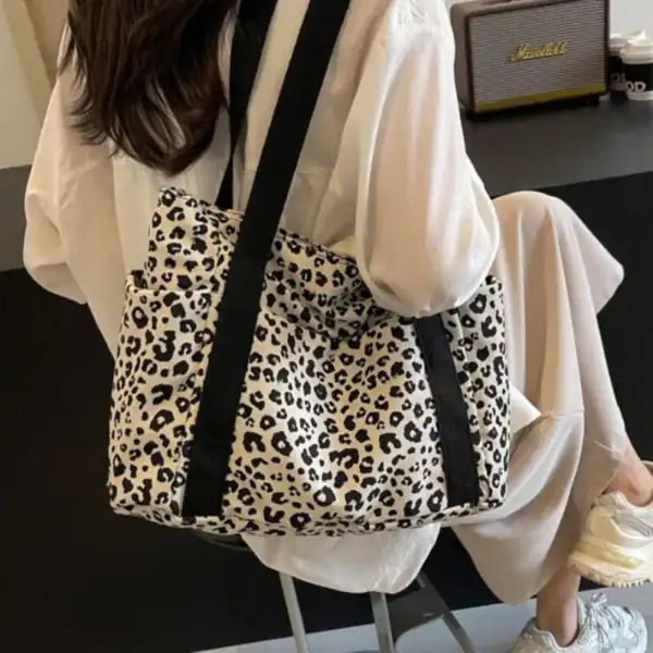 Vit leopard mönstrad axelväska med svarta axelremmar, trendig och stilren.